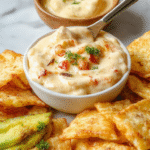 A vibrant bowl of creamy cowboy queso dip with melted cheese, diced tomatoes, jalapenos, and herbs on a rustic wooden table, served with tortilla chips.